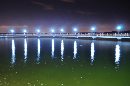 Floating bridge at Changi Beach Singapore by night with slightly starry sky and light reflection on water from lamp post. This bridge is actually a place for people to relax, unwind, and do fishing.の写真素材