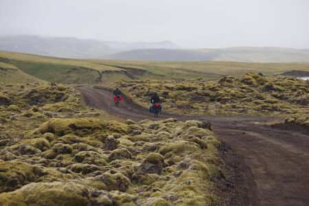 Bikers on road in interior on Iceland, lava fields covered green moss - bicycle trip with panniers in misty dayの写真素材