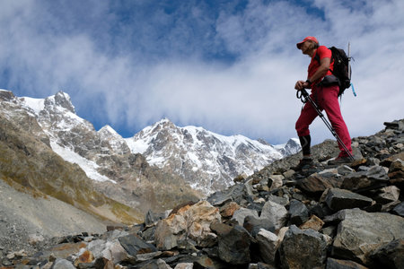 Khalde, Svaneti, Georgia - circa October 2019: Tourist standing on debris of tongue of glacier Khalde. Snowy peaks Dzhangi-Tau and Shkhara in background. Greater Caucasus, Svaneti, Georgiaのeditorial素材
