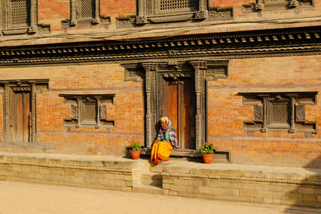 Bhaktapur, Nepal - circa November 2019: Hindu holy woman in traditional colorful dress at entrance of Palace of Fifty-five Windows at Durbar Square, Bhaktapur, Nepalのeditorial素材