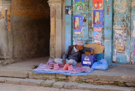 Bhaktapur, Nepal - circa November 2019: An old man sits on the street and sells colorful textile bags. Bhaktapur, Kathmandu Valley, Nepal, Asiaのeditorial素材