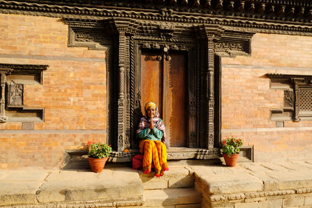 Bhaktapur, Nepal - circa November 2019: Hindu holy woman in traditional colorful dress at entrance of Palace of Fifty-five Windows at Durbar Square, Bhaktapur, Nepalのeditorial素材