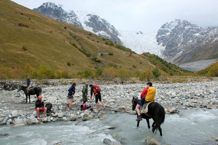 Svaneti, Georgia: circa October 2019: Group of tourists crossing Adishchala river - on foot without shoes or on horseback, during trekking on trail from Khalde to Mulakhi in Greater Caucasus.のeditorial素材