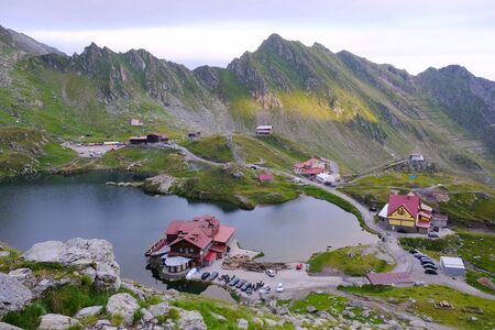 Romania, Romanian Carpathians - Fagaras Mountains, view from the ridge on the lake Balea Lac, houses around and the zigzag road (bends) of the Transfagarasan Highway roadの写真素材