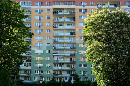 A tall apartment block with balconies, painted colorful among the chestnut trees in bloom. Greenery in the city.の写真素材
