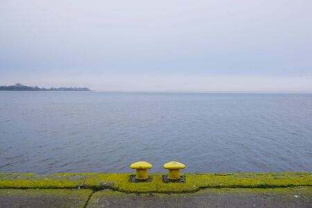Two yellow mooring bollards on empty dock by the lake off season in misty day. Kamien Pomorski,...