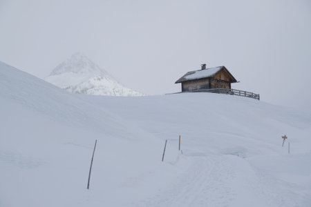 Beautiful winter view of lonely small wooden house in snowy mountains in foggy winter day, when all around is white. Around Alpe di Nemes refuge in Sexten Dolomites, South Tyrol, Italyのeditorial素材