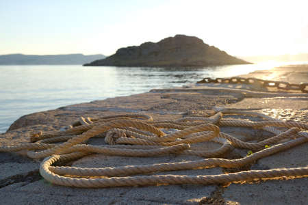 A coiled mooring line on the concrete shore in the light of the setting sun. Island on horizon. Sveti Juraj, Croatia.の写真素材