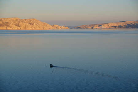 Idyllic view of boat sailing on the sea at dawn. Rocky islands lit by rising sun on horizon. Sveti Juraj, Croatiaの写真素材