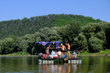 UKRAINE, CANYONS OF DNIESTER - around August 2018: People having fun on primitive raft by the bank...