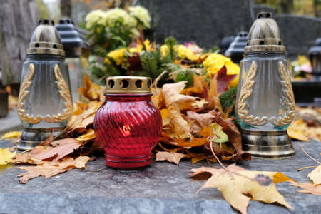 Colorful glass candles among dry autumn leaves on grave in cemetery on November dayの写真素材