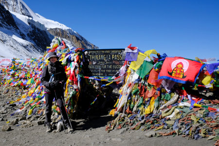 Thorong La Pass, Nepal, Himalaya - circa October 2019: Tourist woman on Thorong La Pass (5416 m) in Himalayas. Plaque and prayer flags. This is the highest place during trekking Annapurna Circuitのeditorial素材