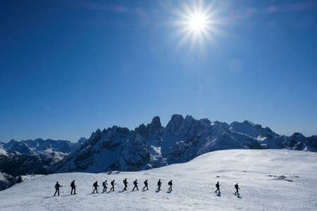 Silhouettes of ski touring tourists walking one by one in beautiful winter sunny scenery. During...