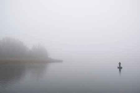 Lonely small boat with fisherman on misty lake in whiteness.の写真素材