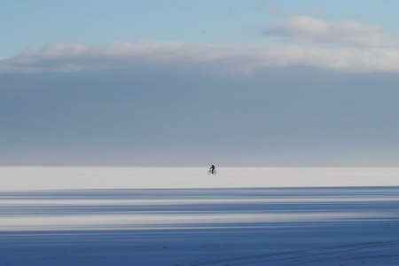 Little silhouette of riding biker on horizon on frozen Baltic Sea in Pucka Bay on winter dayの写真素材