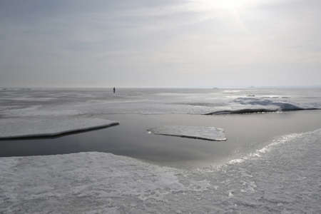 Frozen sea with ice floes is shiny in sun as silver. Silhouette of people on ice. Oslonino,...