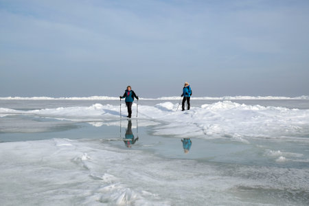 Oslonino, Poland - circa February 2021: Two women are walking on ice floe at sea on beautiful sunny...