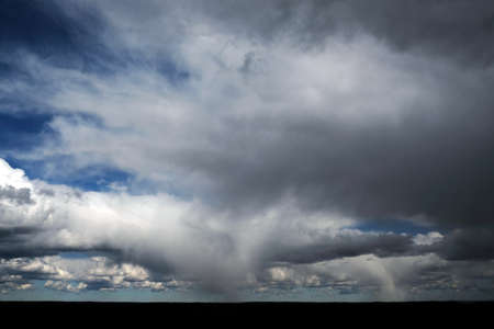 Dramatic sky with dark clouds lit by sun. Black line of horizon.