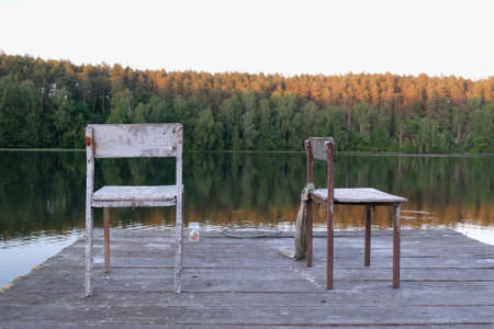 Old wooden pier with two chairs standing on end, in evening lightの写真素材