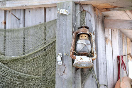 Wall of wooden hut with fishing equipment. There is rustic kerosene lamp and fishing nets.の写真素材