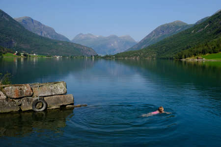 Idyllic view of calm mountain lake and swimming little girl in water. It is Oppstrynsvatn (Strynevatnet, Strynevatn) lake in municipality of Stryn in county of Sogn og Fjord, Norwayのeditorial素材