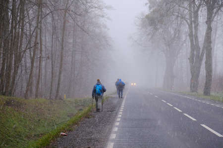 Little snowy asphalt road. Silhouettes of people walking by side of road in snowy misty day.の写真素材