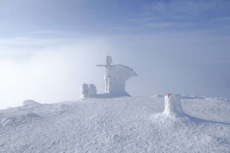 Babia Gora peak in misty winter scenery. Frozen signpost and cross on peak. Diablak, Babiogorski...