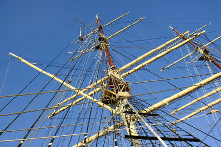 A close-up of the masts and ropes of a sailing ship. Blue sky background.