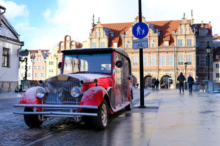 Red retro car in the Old Town of Gdansk. In the background the Green Gate. Poland. Inscription on...