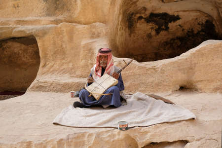 Little Petra (Siq al-Barid), Jordan - circa May 2022: Old Jordanian man in traditional dress with arab rebab string musical instrument in Little Petraのeditorial素材