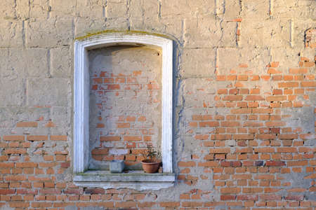 A red brick wall with a bricked up window. There is a flower pot in the window.の写真素材