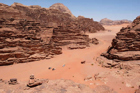 Amazing scenery of Wadi Rum desert with eroded rocks and red sand. Off road cars are standing in valley. Jordanの写真素材