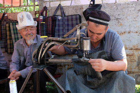 Bishkek, Kyrgyzstan - circa July 2022: A Kyrgyz shoemaker at work in the Osh bazaar in Bishkek.