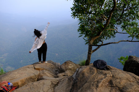 Misty scenery of viewpoint Rock Ella in Sri Lanka with silhouette of standing woman with raised arms in white shirt.の写真素材
