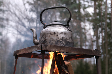 Metal kettle stands on grate over campfire