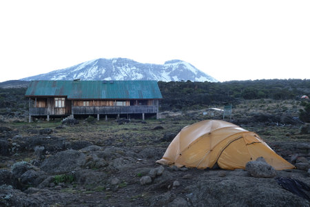 Scenery of Shira Camp on trail to Kilimanjaro with tent, wooden building and silhouette of Mount Kilimanjaro on horizon, Machame Route, Tanzaniaの写真素材