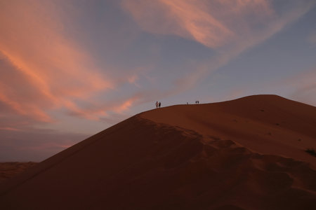 Little silhouettes of people on dune and colorful sunset sky in background, Sahara desert, Moroccoの写真素材