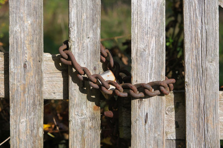 A close-up of a rusty chain and padlock on a wooden fence.