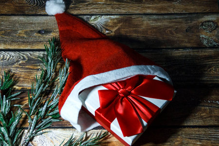 Christmas gift box with red ribbon and Santa hat on wooden background.の写真素材