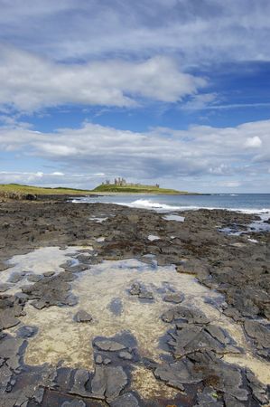Dunstanburgh Castle from the coastal path to Craster with rockpool in the foregroundの写真素材