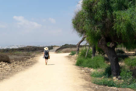 Girl in a hat on a sandy road. Archaeological area, Cyprus. Desert road and green trees. The man on the road.の写真素材