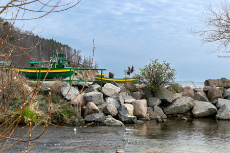 Fishing boat on the seashore in early spring. Stones on the coast. A cliff in the distance.の写真素材