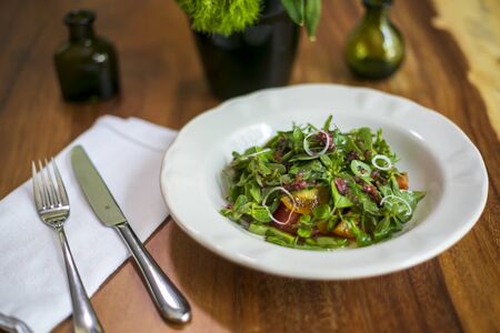 Healthy salad on a white plate on wooden table in an elegant restaurantの写真素材
