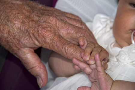 old retired man hand while holding newborn infant handの写真素材