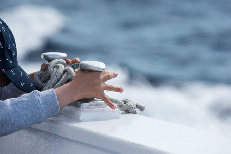 children hands while holding boat bollard on blue sea backgroundの写真素材