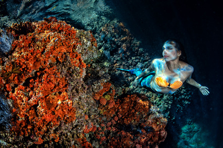 black hair Mermaid swimming underwater in the deep blue sea and looking at youの写真素材