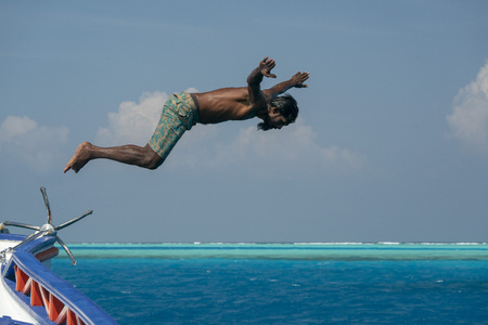 Young maldives man diving from boat in turquoise crystal watersの写真素材