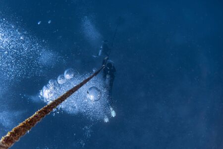 scuba divers while diving in deep blue sea holding a rope