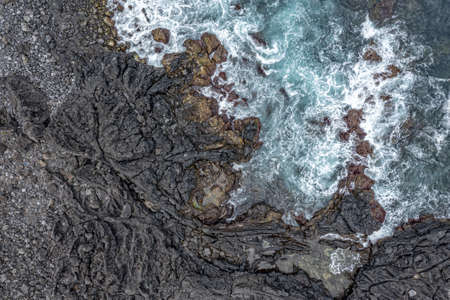 breaking waves of sea in tempest on lava rock cliff drone aerial landscape