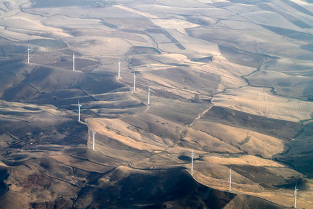 Many Windmill wind turbines near Etna volcano in Sicily and farmed fields aerial view from airplane